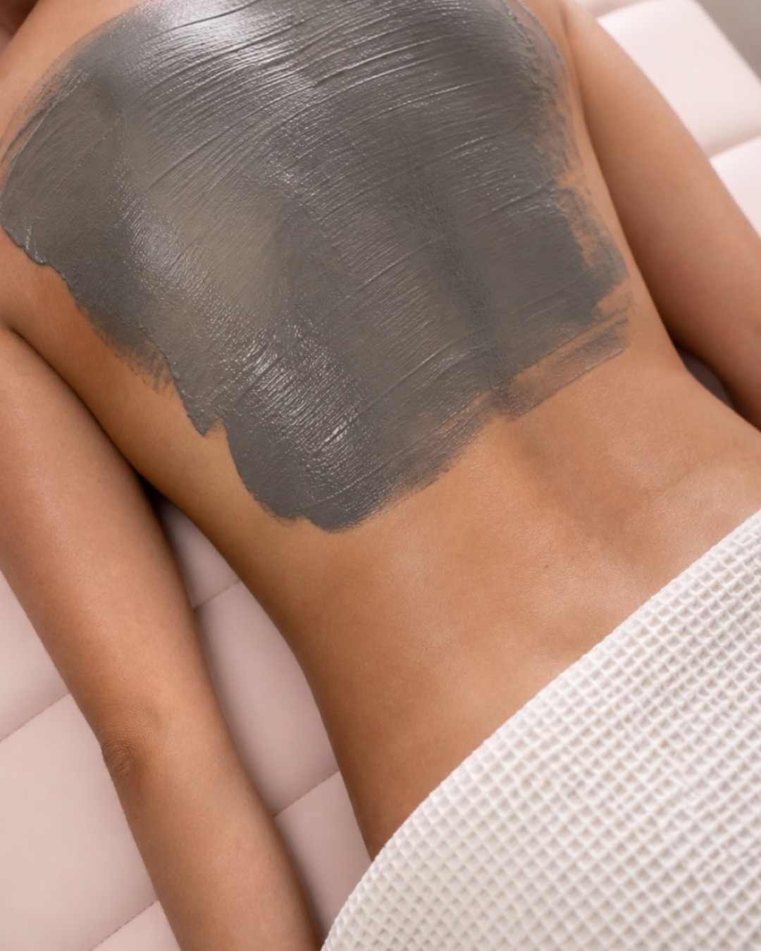 Charcoal mineral mud mask applied across a professionally draped client's back