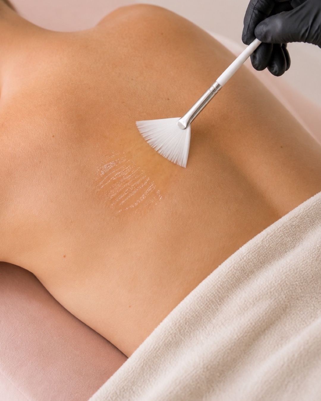 A translucent professional peel applied precisely across a client's back with a fan brush