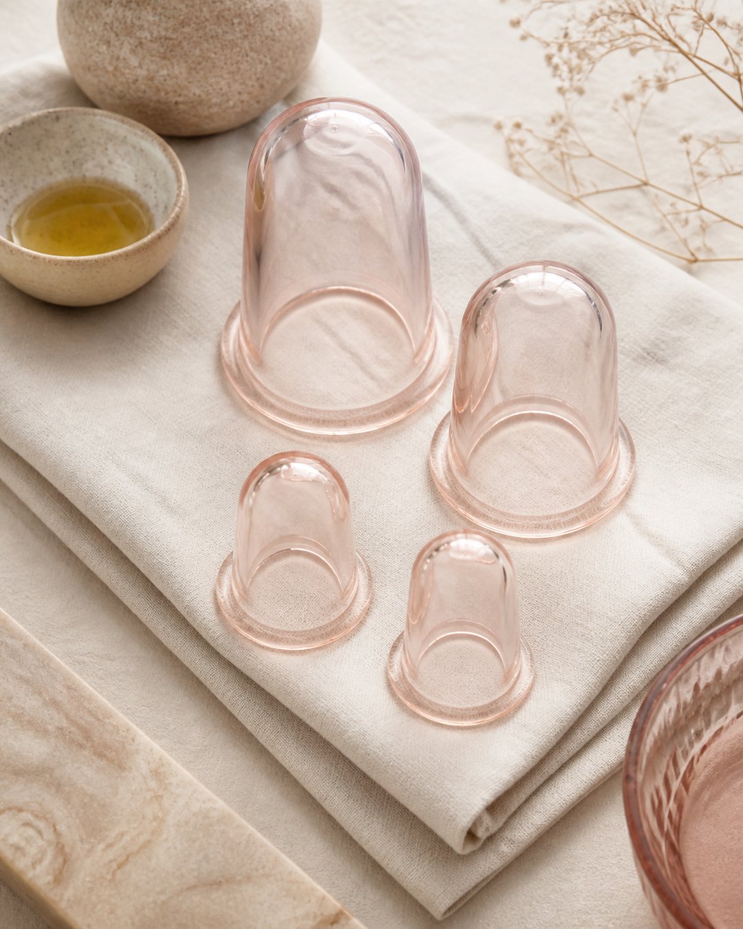 Translucent silicone massage cups and body oil on folded linen